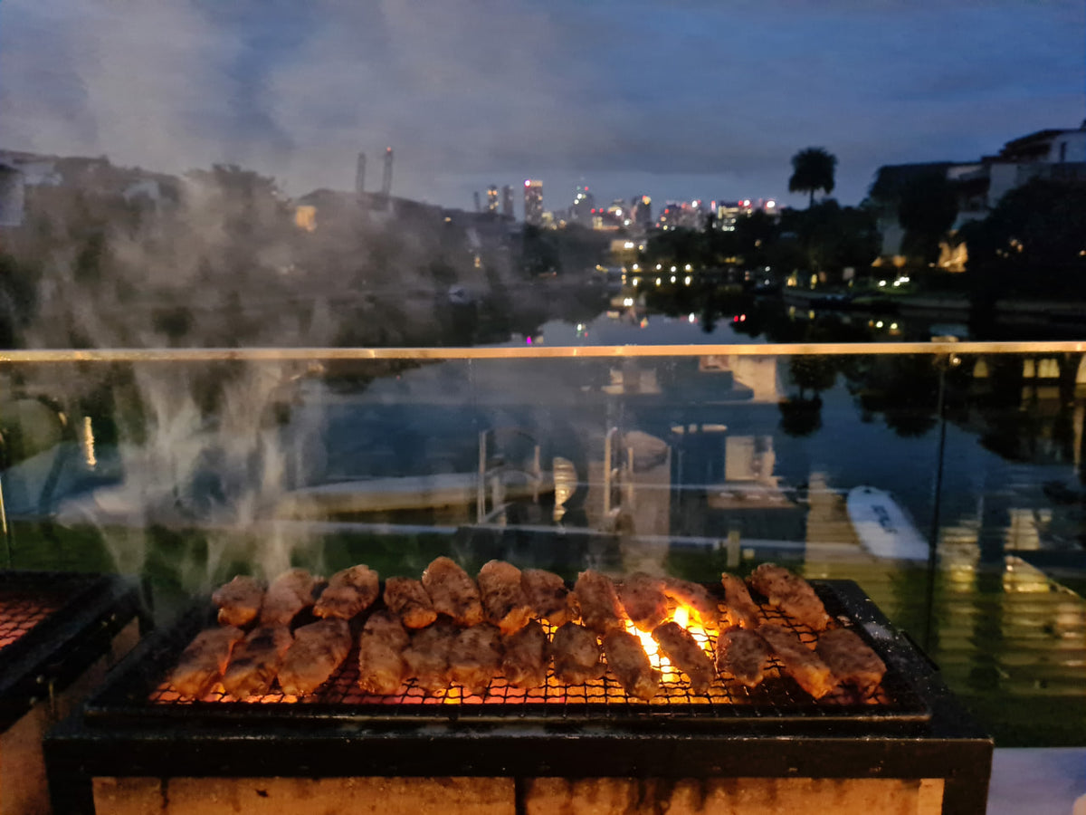 新加坡傍晚水边派对上，Shiok BBQ 现场烧烤炉上摆满肉类