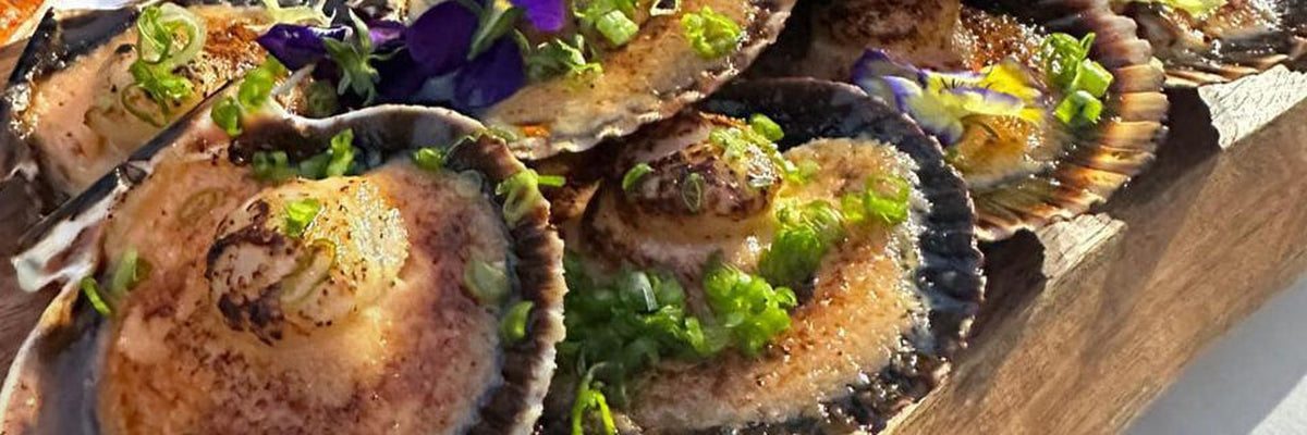 Grilled shellfish in the shell with spring onion on a board from Shiok BBQ Singapore