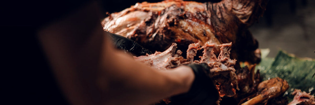 Gloved hands pulling roast meat off the bone at a Shiok BBQ live station in Singapore