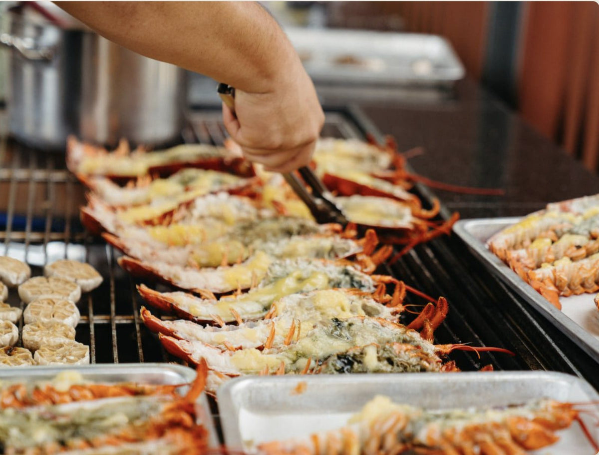 Butter garlic lobster halves and roasted garlic on the grill at a Shiok BBQ live station, Singapore
