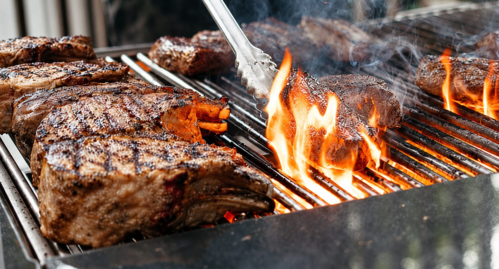 Pork chops and steaks searing over open flame on the grill at a Shiok BBQ live station in Singapore